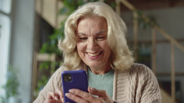 An old woman looks at photographs on the phone. She likes them from what she laughs