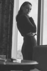 Young caucasian woman, standing by the window wearing a brown dress sweater in modern style room