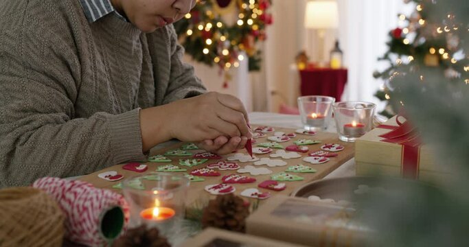 Asia happy adult people woman enjoy make craft gift for Xmas eve party snack cooking food recipe on kitchen table in good warm time. Cute smile gingerman bakery icing sugar with red green white color.