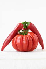 Red tomato, two red chili peppers on white table