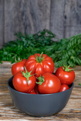 Red tomatoes in bowl on rustic wooden table against green carrot tops