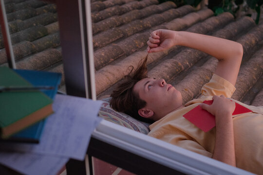 Young student laying holding a book playing with hair