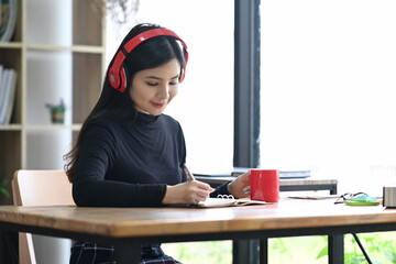 Peaceful asian woman wearing headphone and writing her diary.