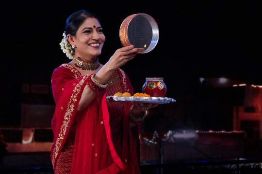Woman looking at moon through a sieve during Karva Chauth
