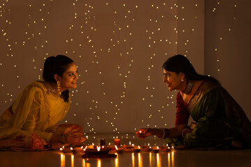 Mother and daughter placing diyas around rangoli on Diwali