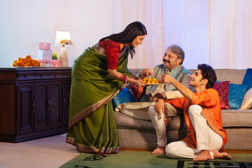 Woman giving ladoos to her husband and son on Diwali