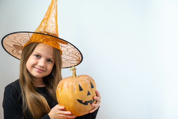 Portrait of little girl in witch costume holding pumpkin with Jack O Lantern face. Kid in orange...