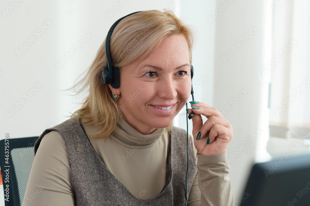 Wall mural a businesswoman sitting in front of a computer with a headset and a camera communicates via video. c