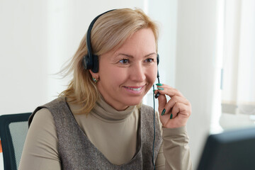 A businesswoman sitting in front of a computer with a headset and a camera communicates via video....