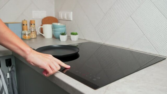 Modern kitchen appliance. Woman hand turn on induction stove to cook. Finger touching sensor button on induction or electrical hob