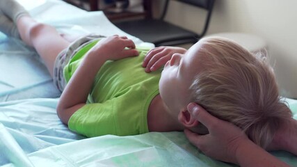 A 4 years old caucasian boy is laying on the bed at manual therapist who is holding his head. A boy in osteopath's cabinet on the bed receiving manual therapy - Powered by Adobe