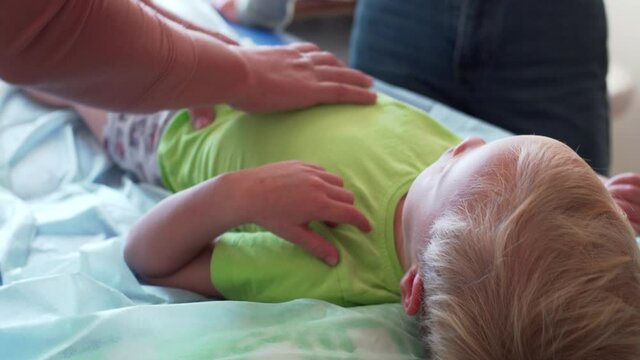 A caucasian boy is laying on the bed at manual therapist who touching and movig his body, checking out his tummy and ribes. A boy in osteopath's cabinet on the bed receiving manual therapy