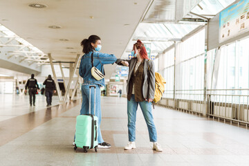Young multiracial women in face masks elbow bumping at train station