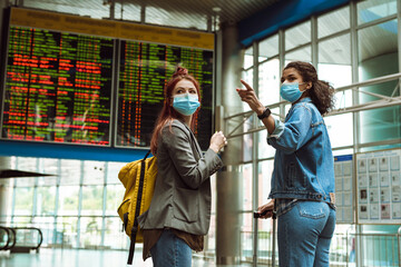 Multiracial two women in face mask pointing finger aside at train station