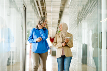 Two smiling female colleagues walking in office hall