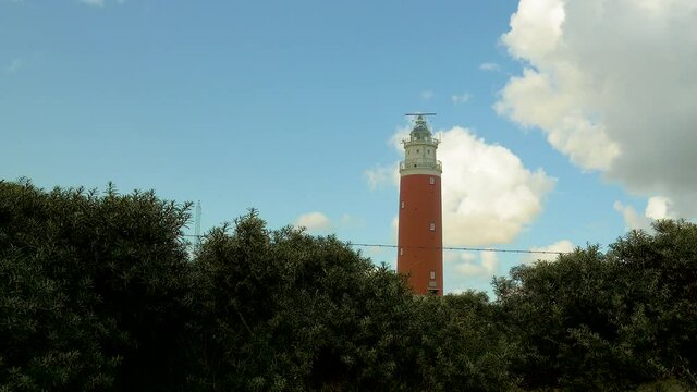 wide angle steady shot of sea ​​buckthorn in the foreground. In the background a lighthouse in the dunes. The sky is blue with beautiful clouds passing by.