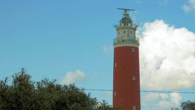 wide angle steady shot of sea ​​buckthorn in the foreground. In the background a lighthouse in the dunes. The sky is blue with beautiful clouds passing by.