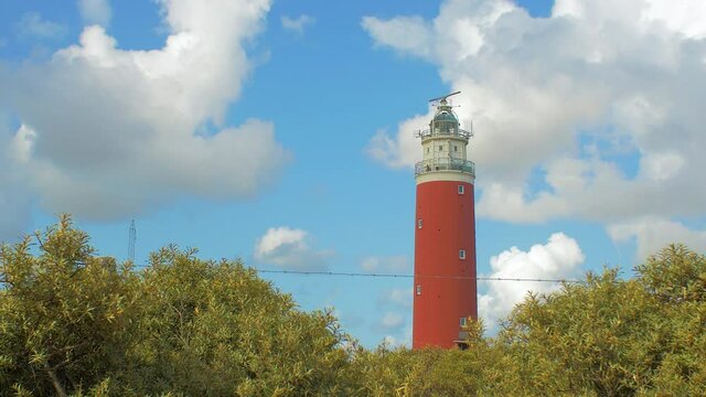 wide angle steady shot of sea ​​buckthorn in the foreground. In the background a lighthouse in the dunes. The sky is blue with beautiful clouds passing by.