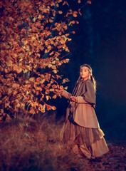 Young girl in national costume in the mystery fall night forest