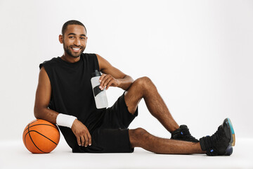 Fototapeta premium Young black sportsman drinking water while posing with basketball