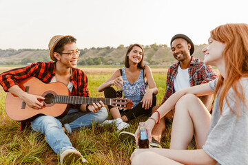 Multiracial friends smiling and playing guitar while sitting on grass