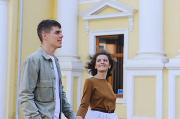 Fototapeta premium Love story of stylish funny couple: young man in a t-shirt. And a cute young woman in wedding white skirt and yellow sweater. Family holiday and togetherness, date.