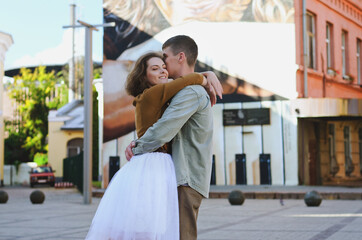 Obraz premium Love story of stylish funny couple: young man in a t-shirt. And a cute young woman in wedding white skirt and yellow sweater. Family holiday and togetherness, date.