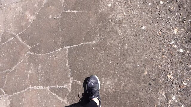 Footsteps of a woman walking on a road of dirt. She is wearing black shoes and black pants.