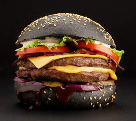 Big black burger with beef cutlet, cheese and bacon on a black background. Side view, close-up