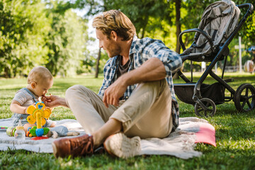 White father feeding his son while resting on blanket at park