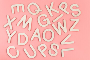 Wooden alphabet letters on pink paper background.