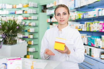 Ordinary woman pharmacist is standing welcoming near cashbox in pharmacy