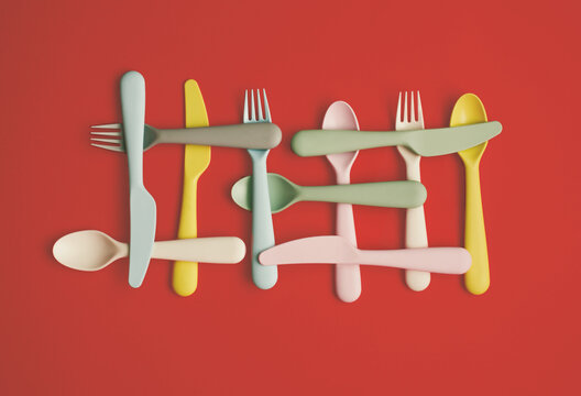 Plastic spoons, fork and knifes lay down onm pastel red background. Flat lay horizontal composition, creative minimal diet cutlery concept