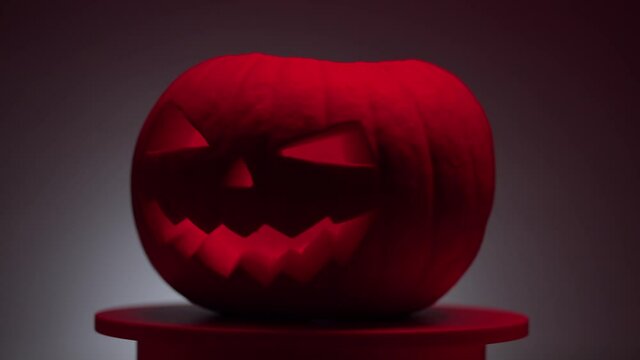 continuous looping dark halloween pumpkin with carved teeth, eyes and nose on a rotating round light platform on a gray background