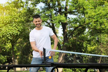 Happy man playing ping pong outdoors on summer day