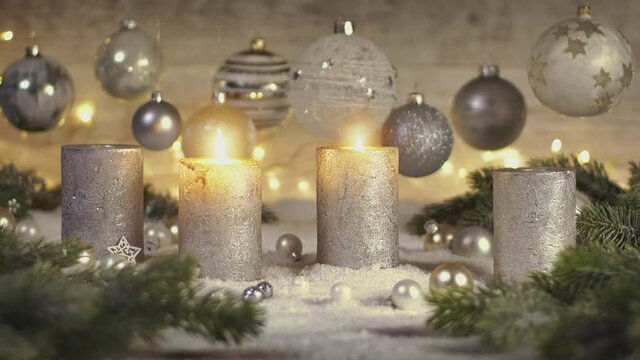 Elegant advent decoration with fir branches on snow and four candles with the flames appearing one after the other, decorated with bokeh lights and baubles hanging in the background