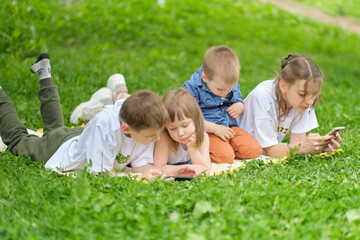 Naklejka na ściany i meble children friend group playing internet with mobile smartphone on grass. Happy children using smartphones sitting on the grass. Brothers and sister.