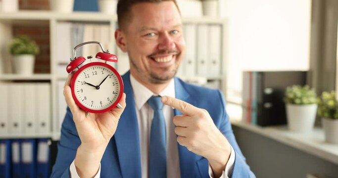 Young smiling businessman showing time on alarm clock with his forefinger 4k movie