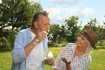 Lovely mature couple spending time together in park. Man blowing soap bubbles