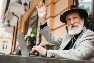 White senior man gesturing while working with laptop in cafe