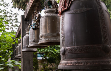 Many metallic bells hanging in a row on wooden pillars outside in thai buddhist temple. Lined with...