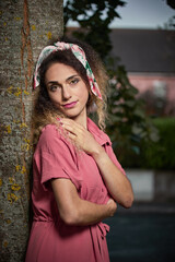 vertical portrait of a young woman leaning on a tree in a pink pin-up dress
