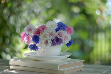 Colorful bunch of cornflowers in a white cup on blurred background in the summmer garden
