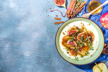 Autumn breakfast or snack, spicy semolina porridge with caramelized apples, grilled peach, plums and figs, nut, thyme, honey. Top view on blue sun lighted concrete table