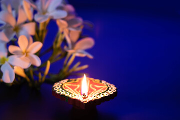 Handcrafted Eco Friendly Clay Diya Deep Dia Glowing With White Flowers On Blue Background. Indian Festival Theme For Diwali Pooja, Navratri, Dussehra Puja, Happy New Year, Deepawali Or Shubh Deepavali © Rangeecha