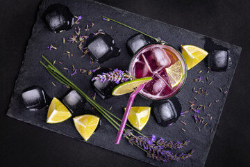 Fresh homemade lemonade with lavender and ice. Delicious purple icy cold party drink on slate board with dark background.