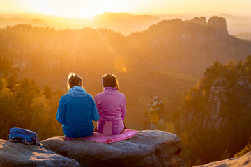 Couple in colorful jackets enjoying sunset atop the viewpoint in the mountains. Romantic mood of evening Saxon Switzerland.