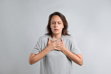 Mature woman suffering from breathing problem on light background