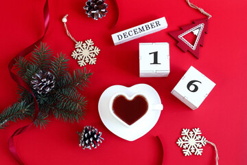 Fototapeta na wymiar Calendar for December 16: the name of the month in English, cubes with the number 16, a cup of tea in the shape of a heart, a fir branch, cones, Christmas decor on a red background, top view