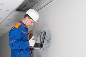 a master in a blue uniform, laid the wiring for the Wi-Fi router in a hidden false ceiling system and verifies the correct installation via a laptop, there is a place for an inscription, close-up